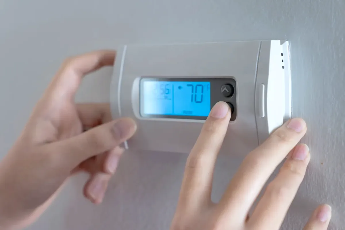 Hands adjusting a digital wall thermostat